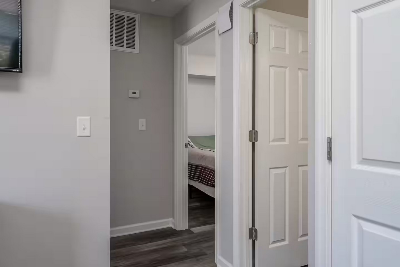 Hallway with multiple doors, grey walls, and dark wood flooring leading to bedrooms.