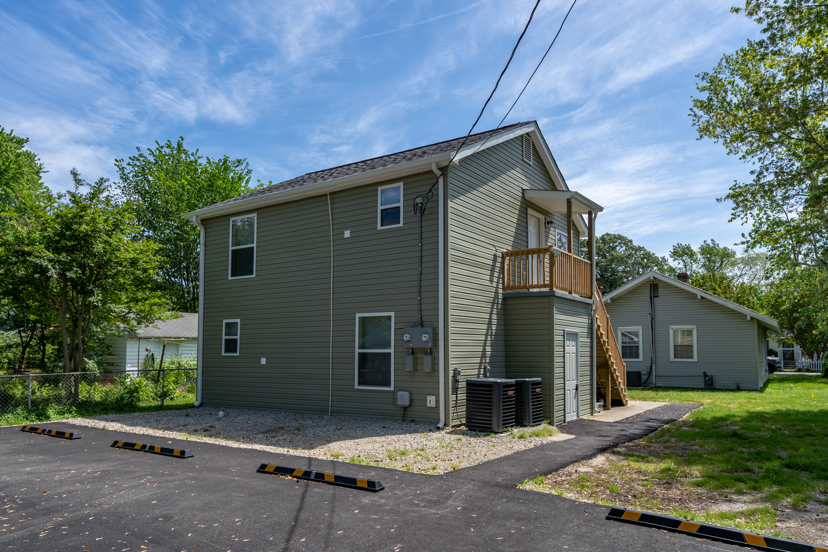 Back view of a two-story duplex with parking spaces and a fenced yard.