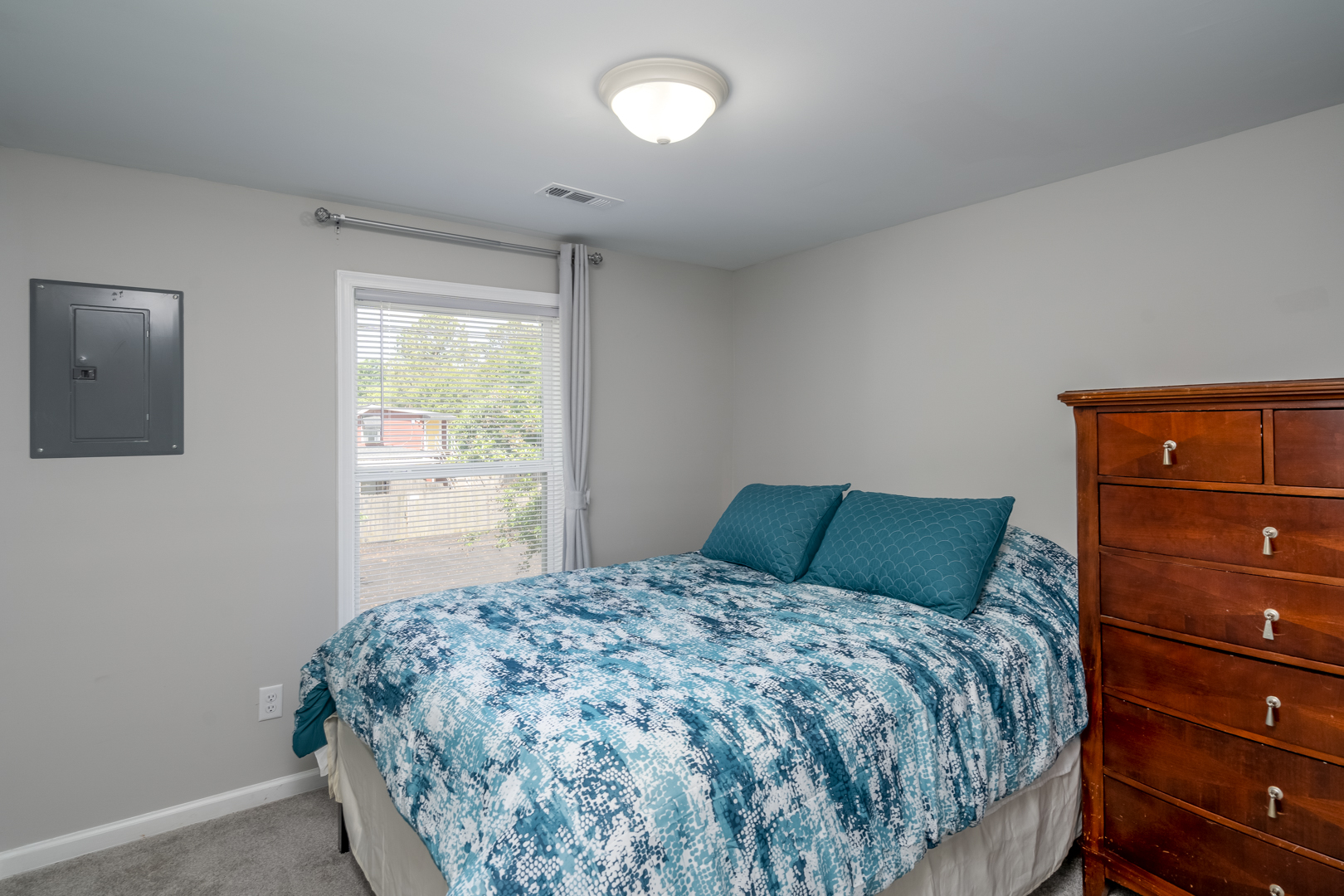 Bedroom with a blue and white bedspread, wooden dresser, and large window.