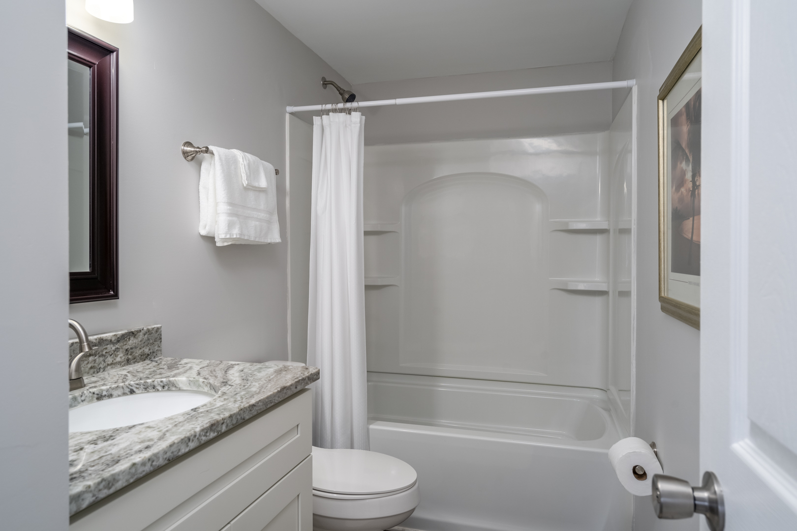 Bathroom with a granite countertop, white vanity, and a bathtub with shower curtain.