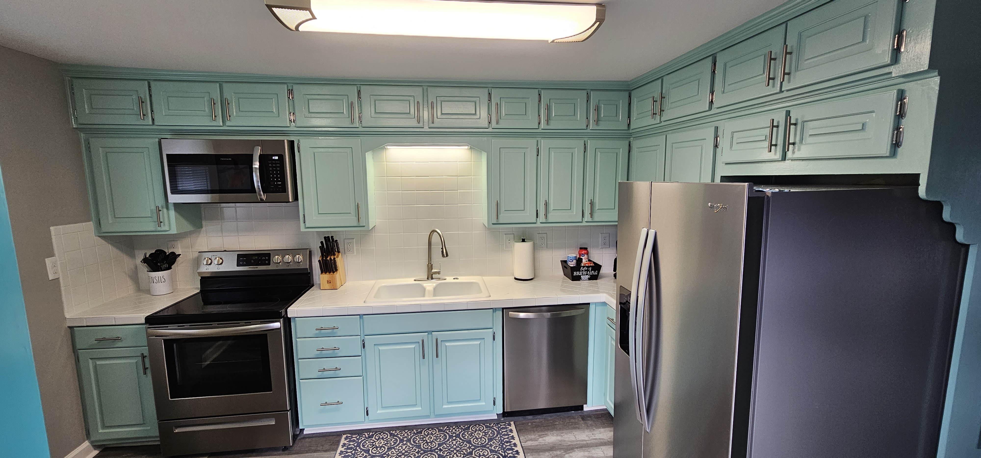 Kitchen with teal cabinetry, stainless steel appliances, and white tile backsplash