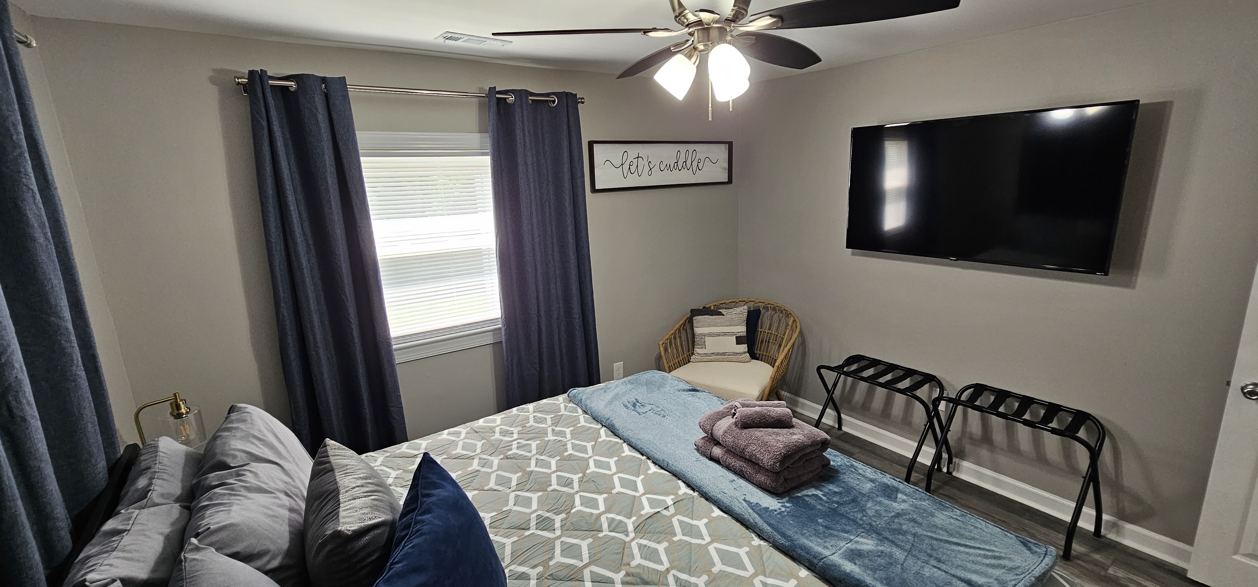 Bedroom with plush bedding, dark curtains, and a mounted TV