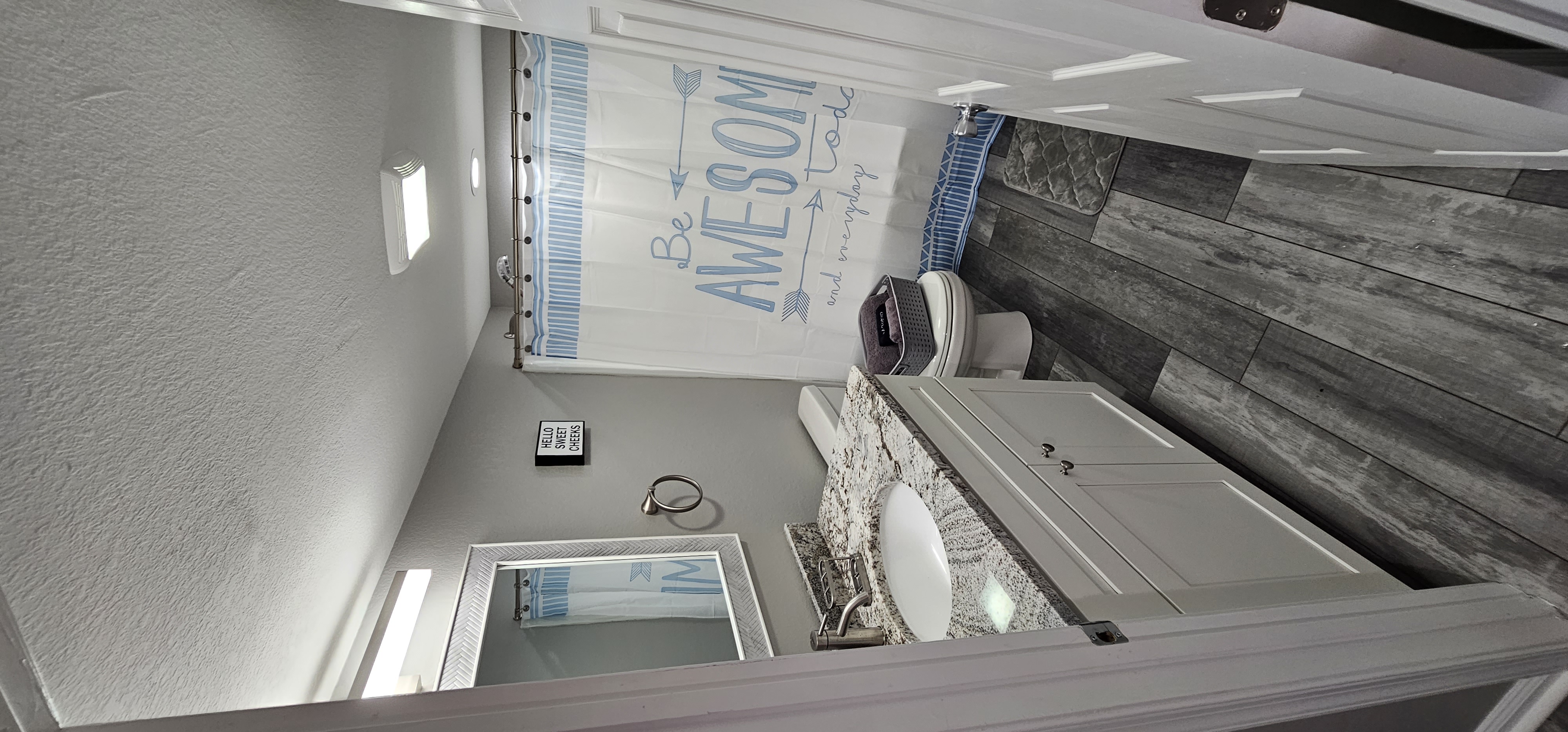 Modern bathroom with a granite countertop, white vanity, and a motivational shower curtain.