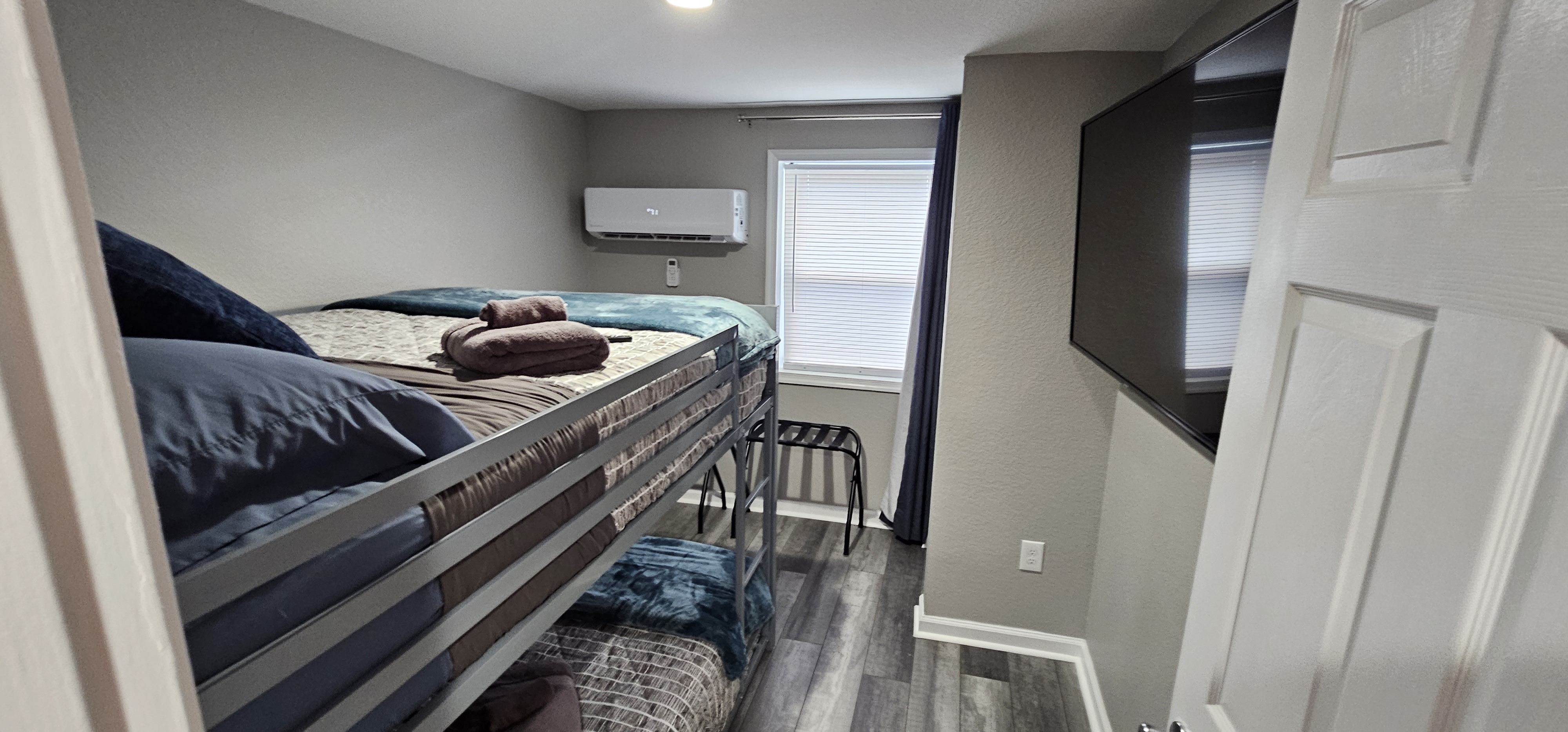Side view of a bedroom featuring a bunk bed, window blinds, and a wall-mounted air conditioning unit.