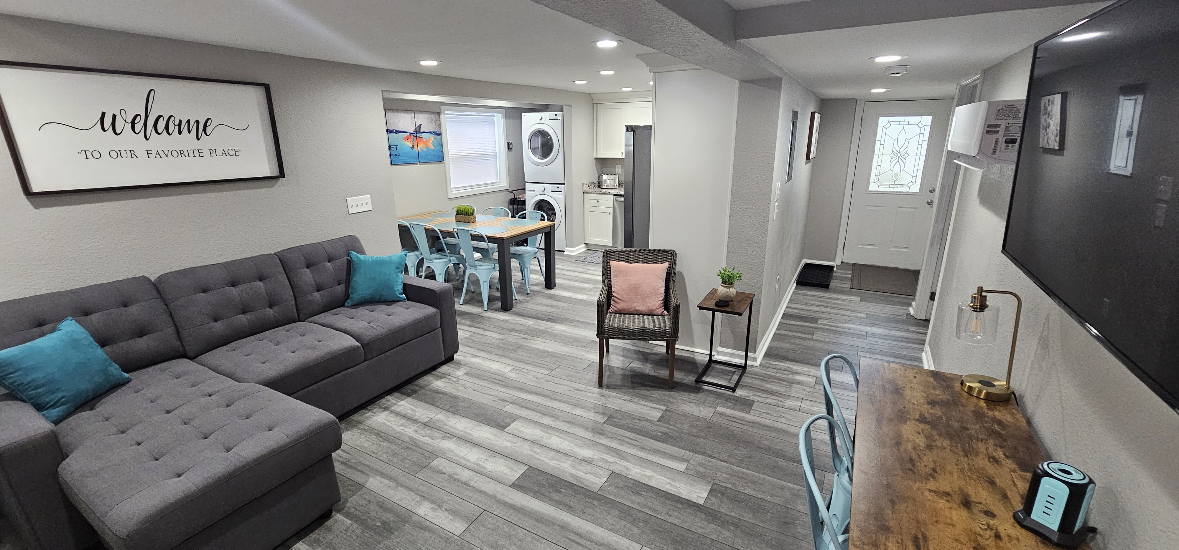 Another angle of the living room showing a cozy seating area and work desk with a mounted TV.