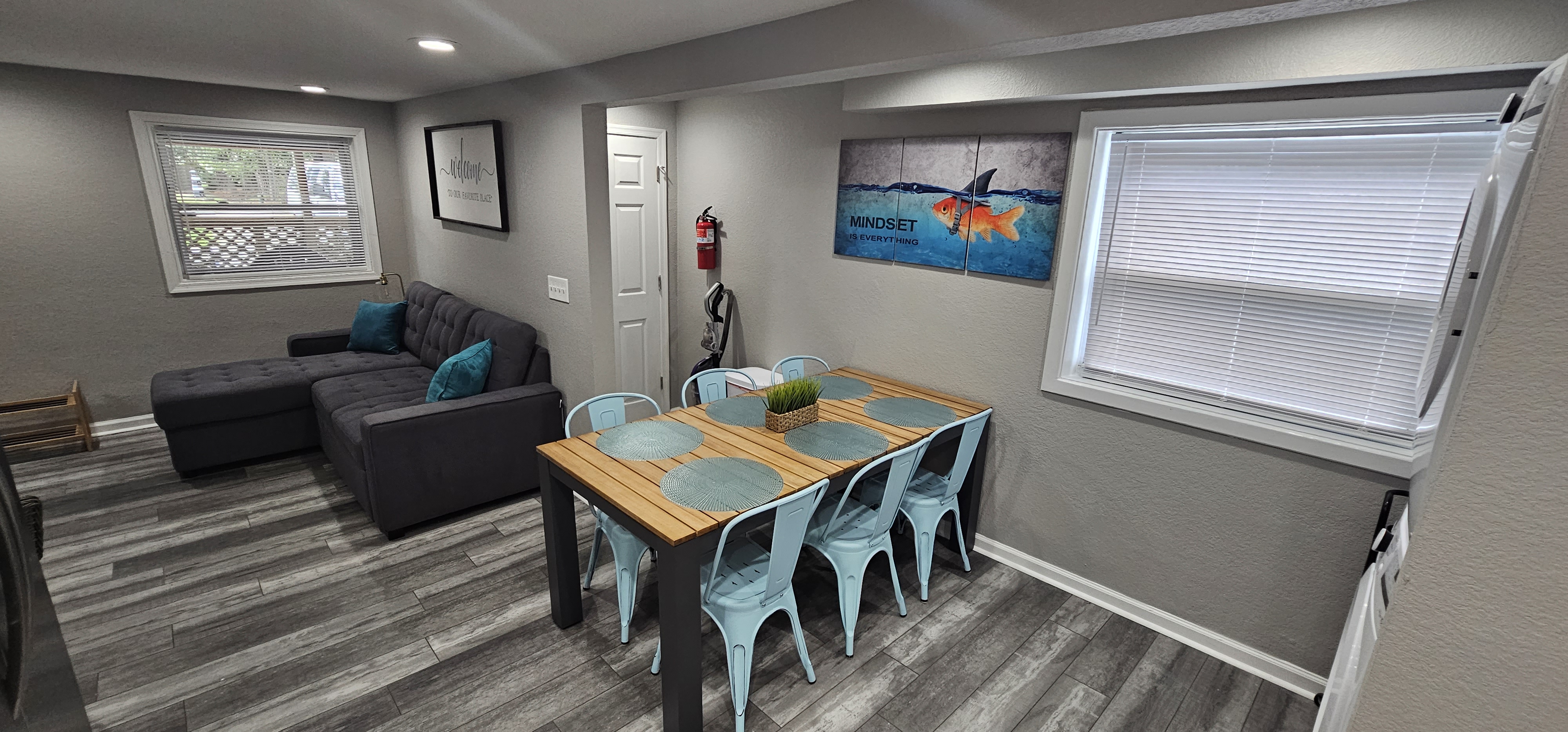 Dining area with a wooden table, metal chairs, and a motivational wall art of a goldfish with a shark fin.