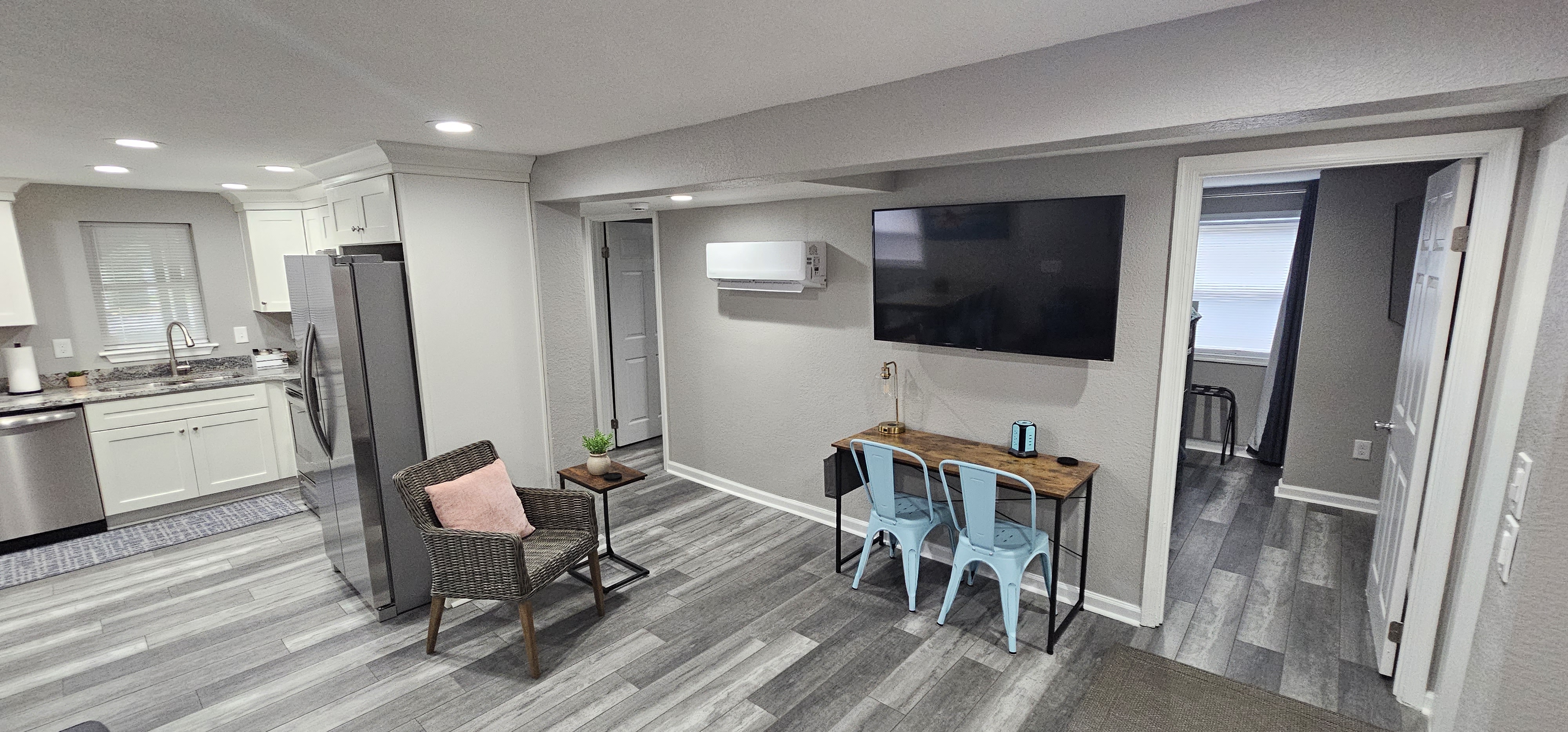 Small work area with a wooden desk, two metal chairs, and a mounted flat-screen TV.
