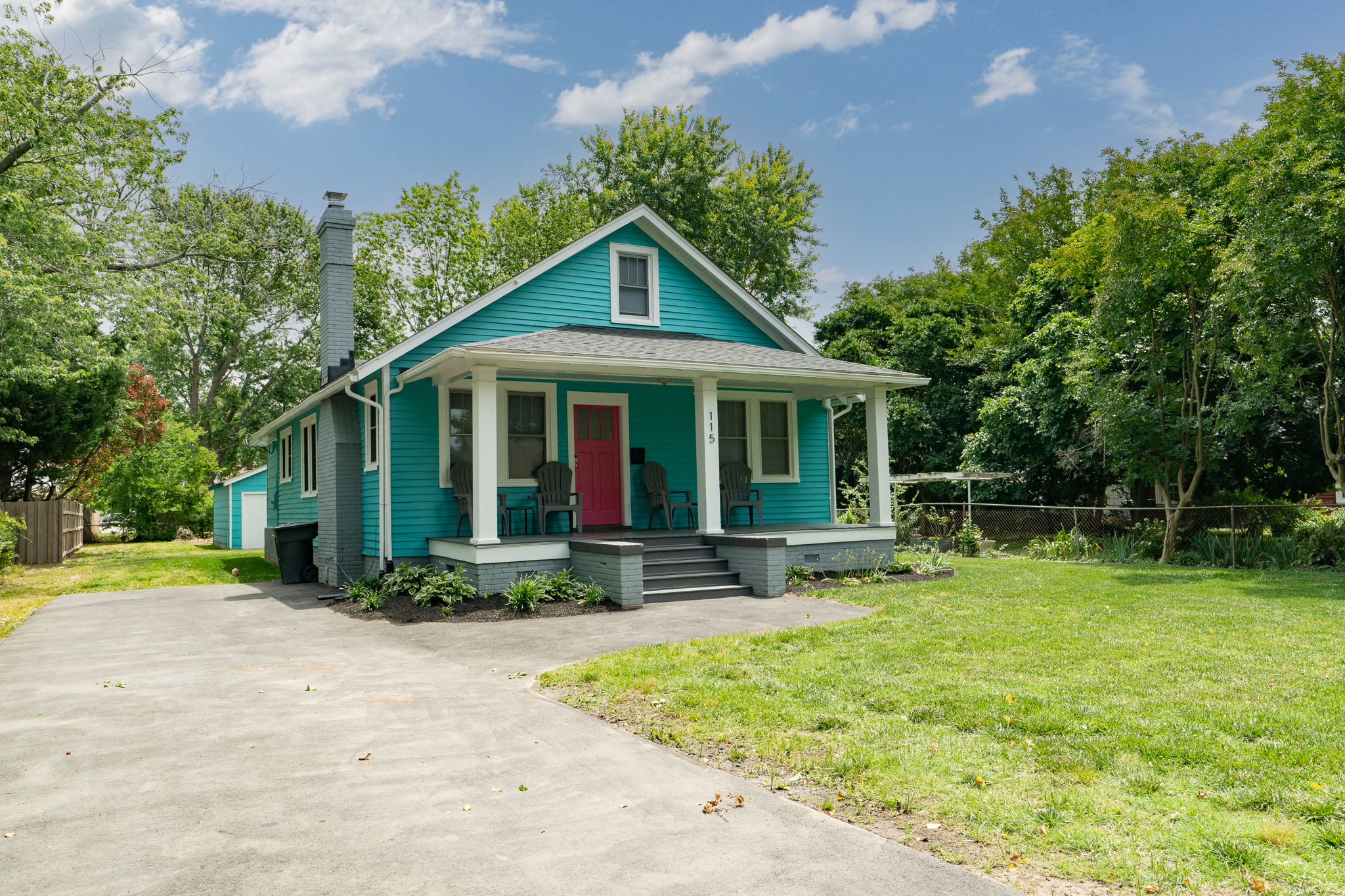 Angled view of a cozy turquoise bungalow with a spacious front yard and driveway.