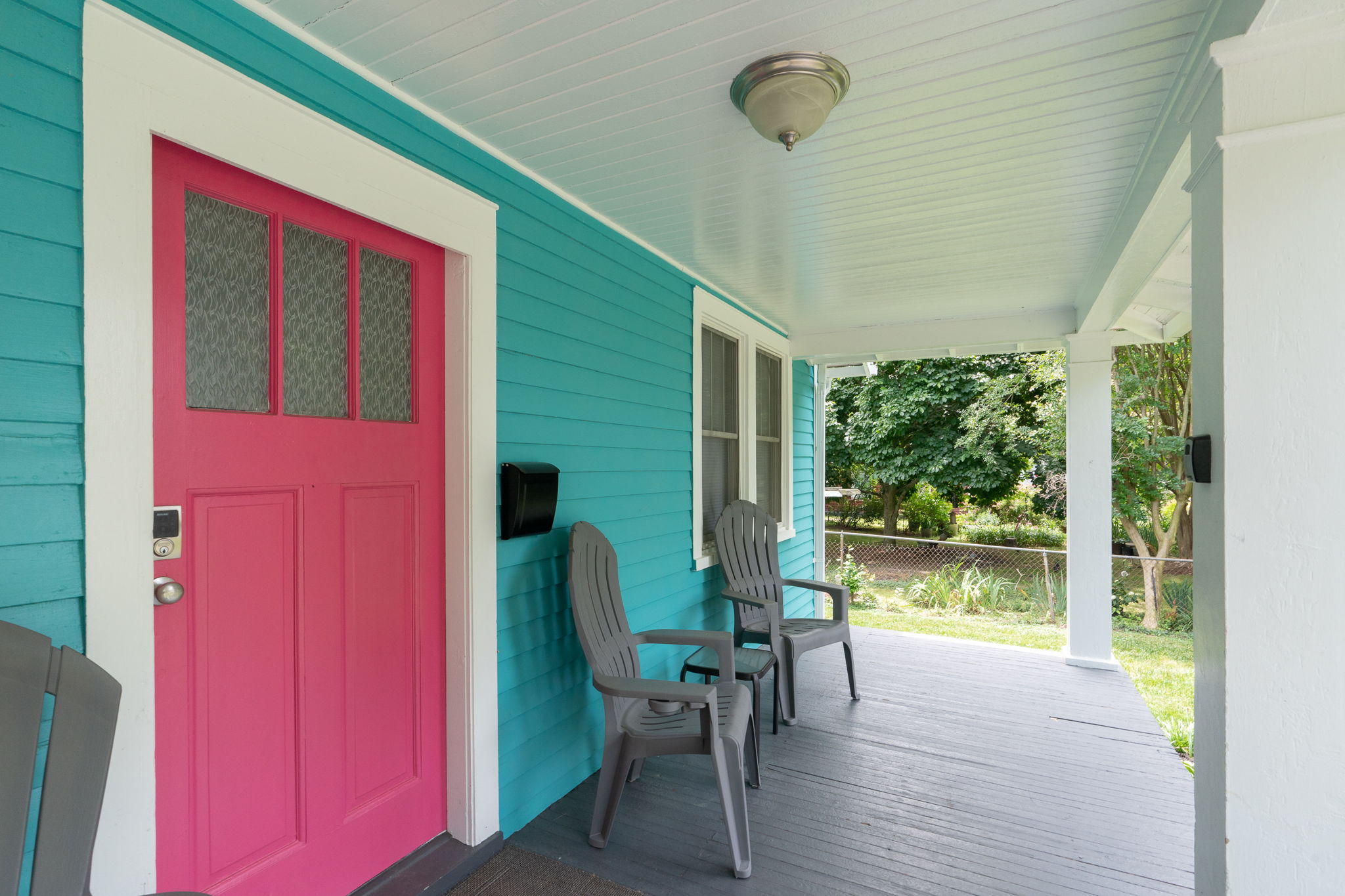 Close-up of a bright pink front door with seating on a covered porch.