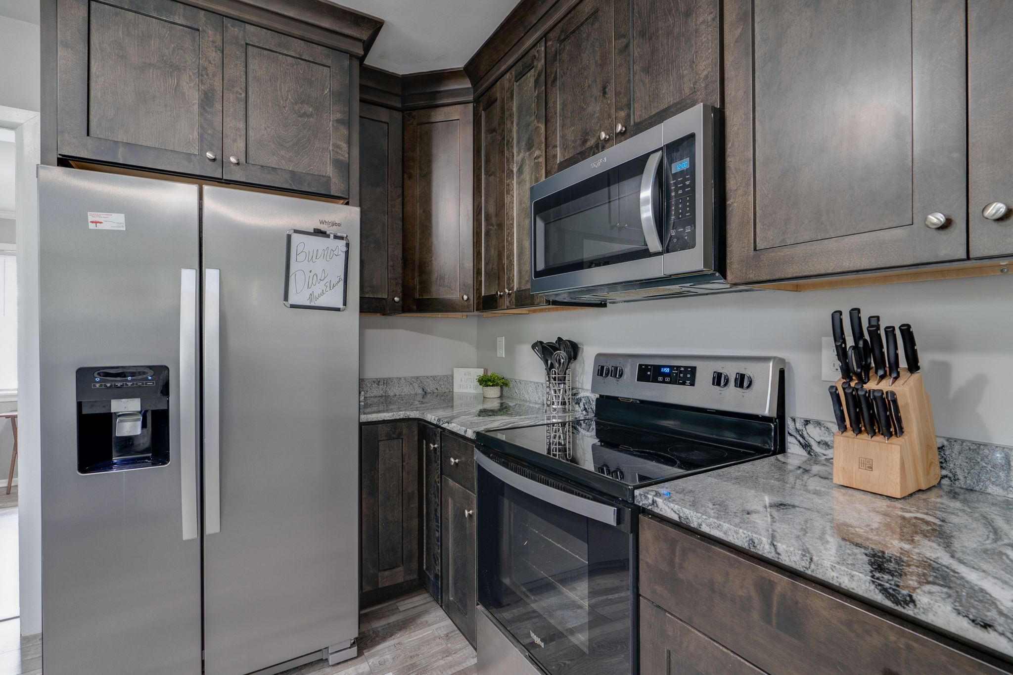 Corner view of a kitchen featuring a sleek refrigerator and oven with dark cabinetry.