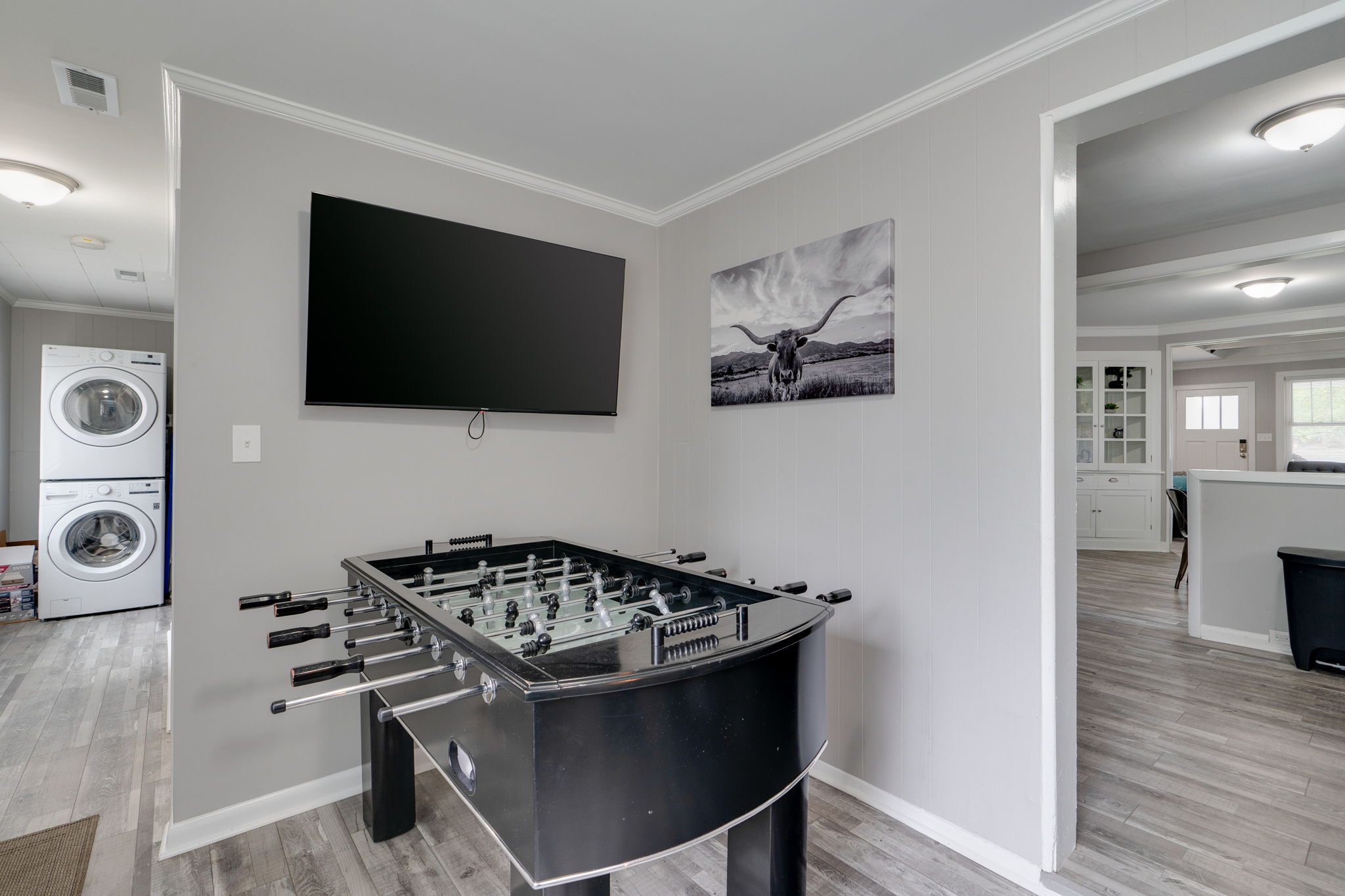 Entertainment area with a foosball table, wall-mounted TV, and a laundry room in the background.