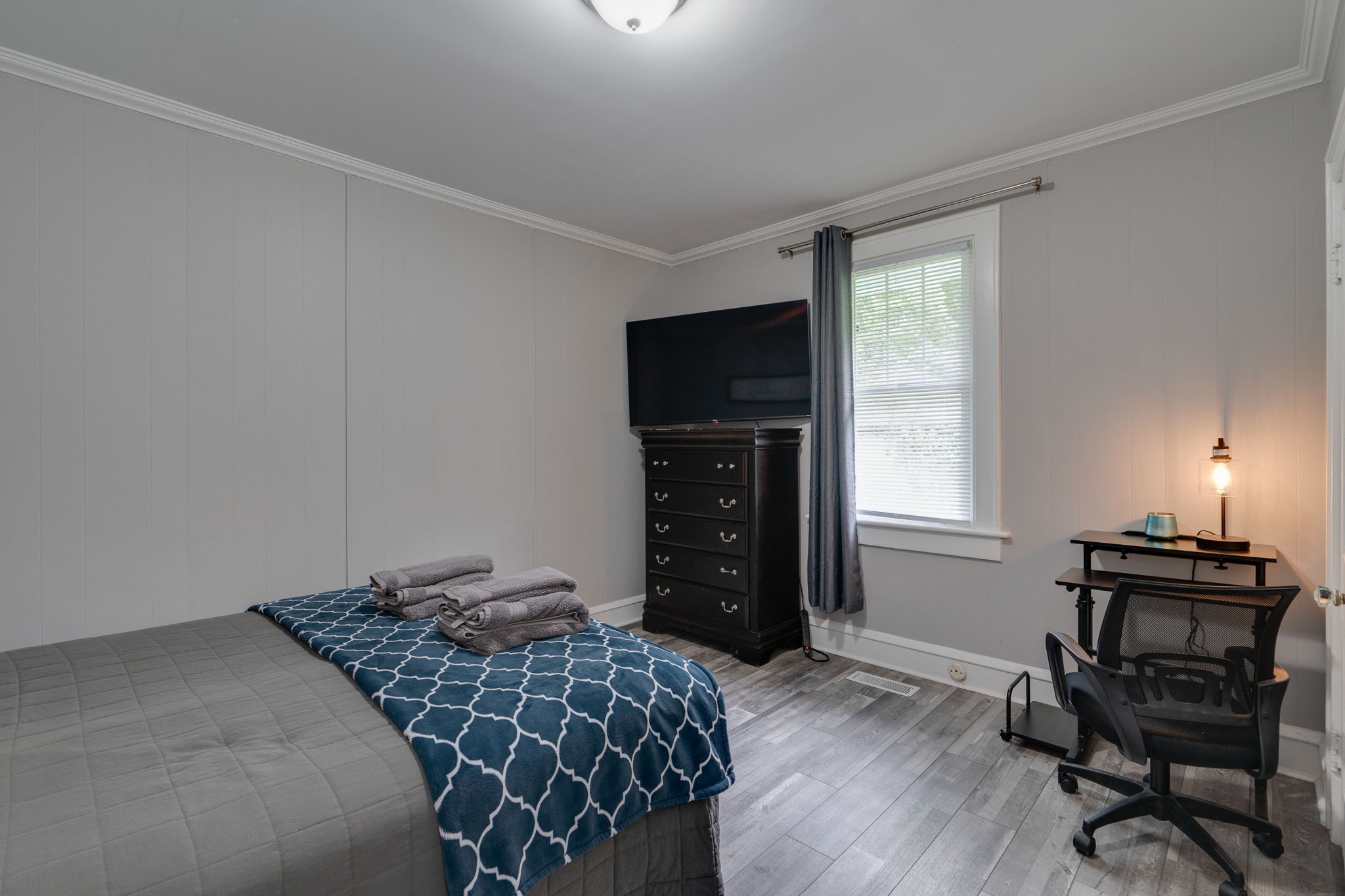 Cozy bedroom with a bed, TV, dresser, and a small workspace with a desk and chair.