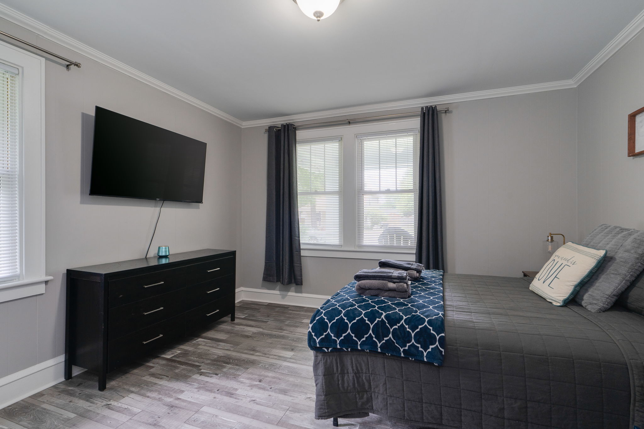 Second bedroom with a large bed, wall-mounted TV, and dark furniture.