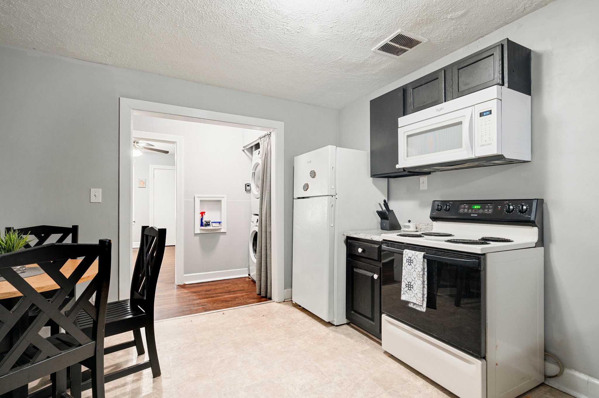 Kitchen with white appliances, black cabinets, and a dining table.