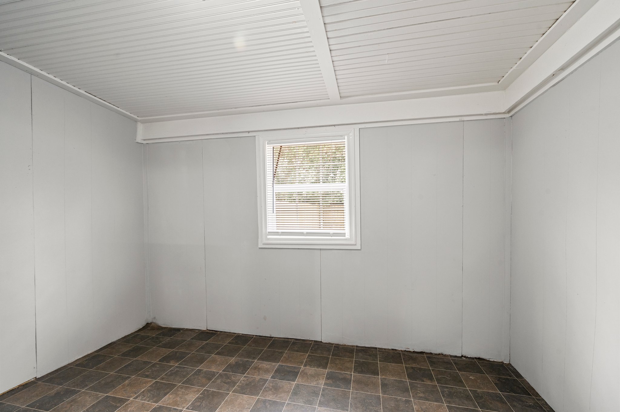 Empty sunroom with tiled flooring and a single window.