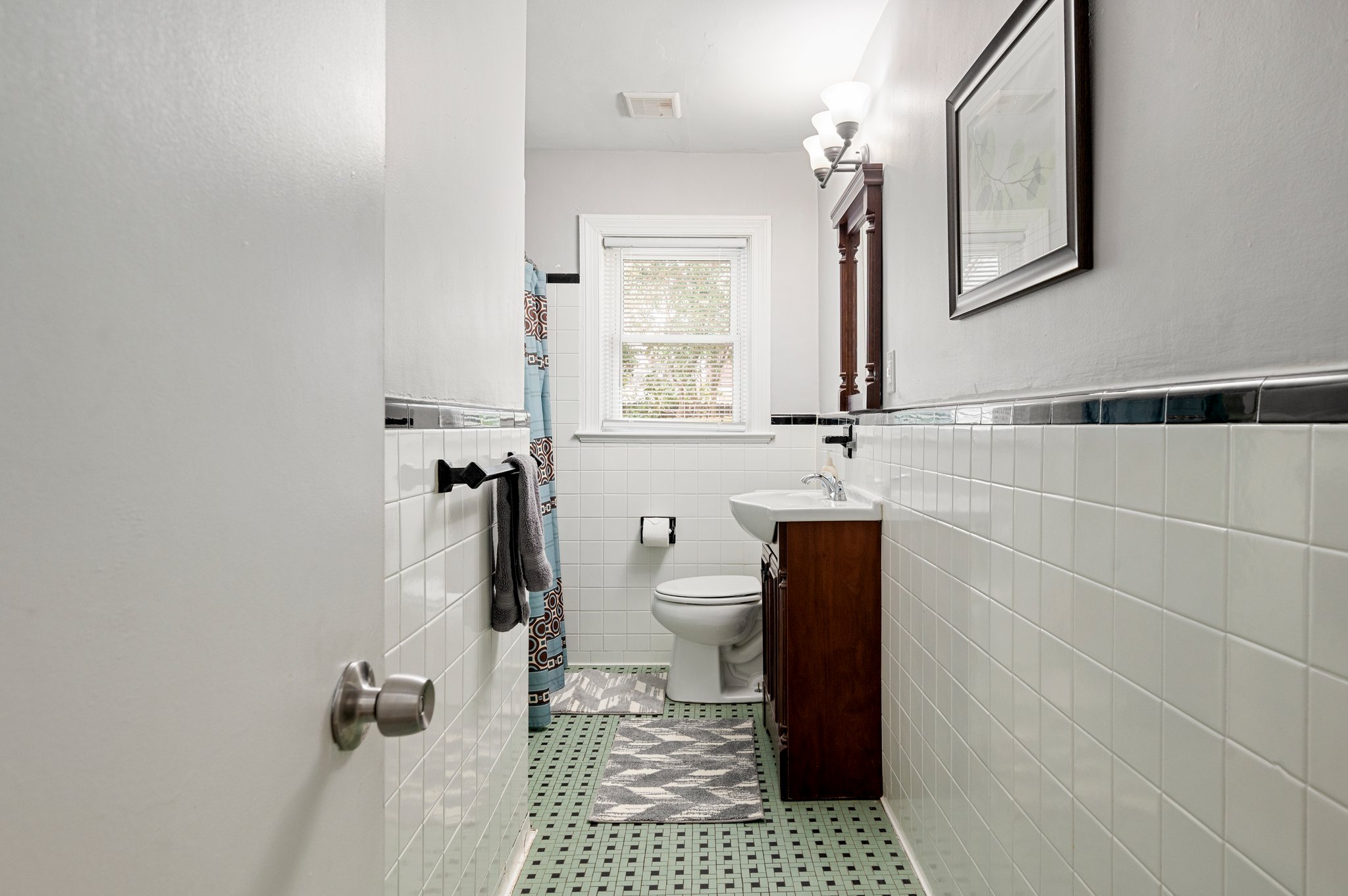 Bathroom with white tile walls, a window, and a vanity with mirror.