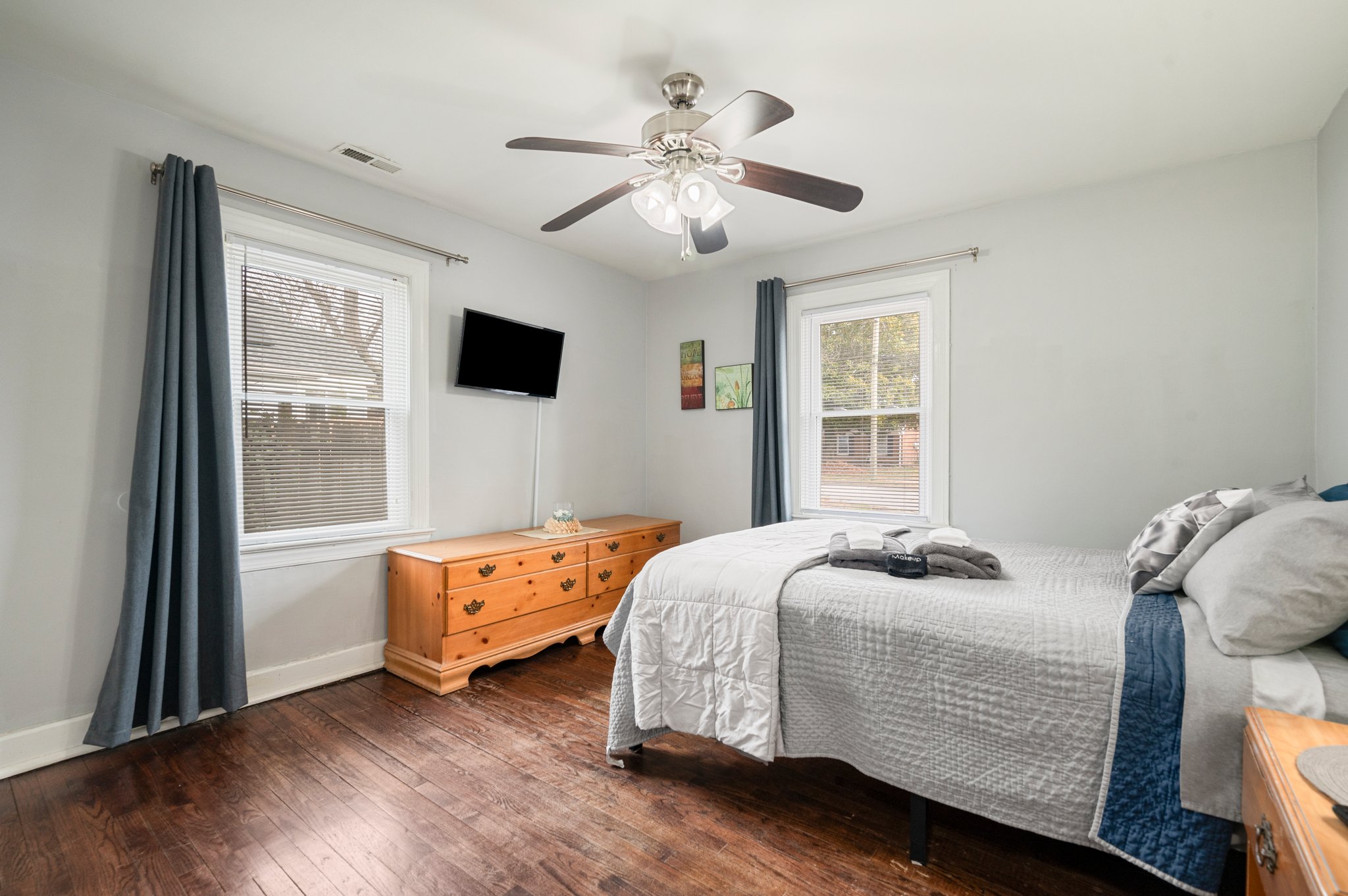 Bedroom with a queen bed, wooden dresser, and a wall-mounted TV.