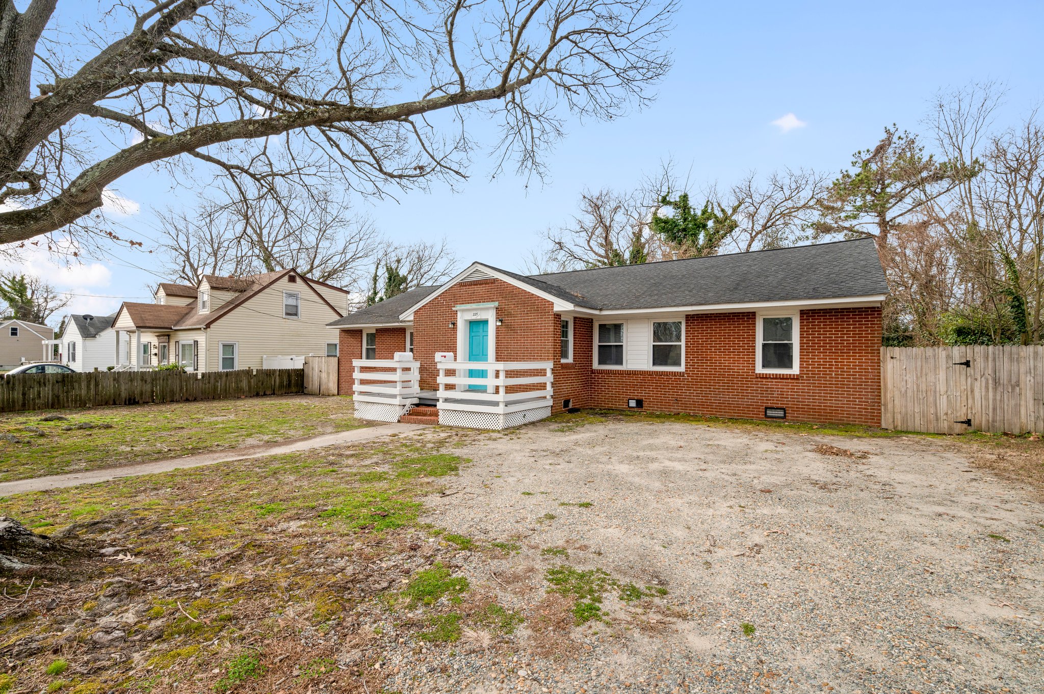 Angled front view of a brick duplex with a gravel driveway and fenced yard.