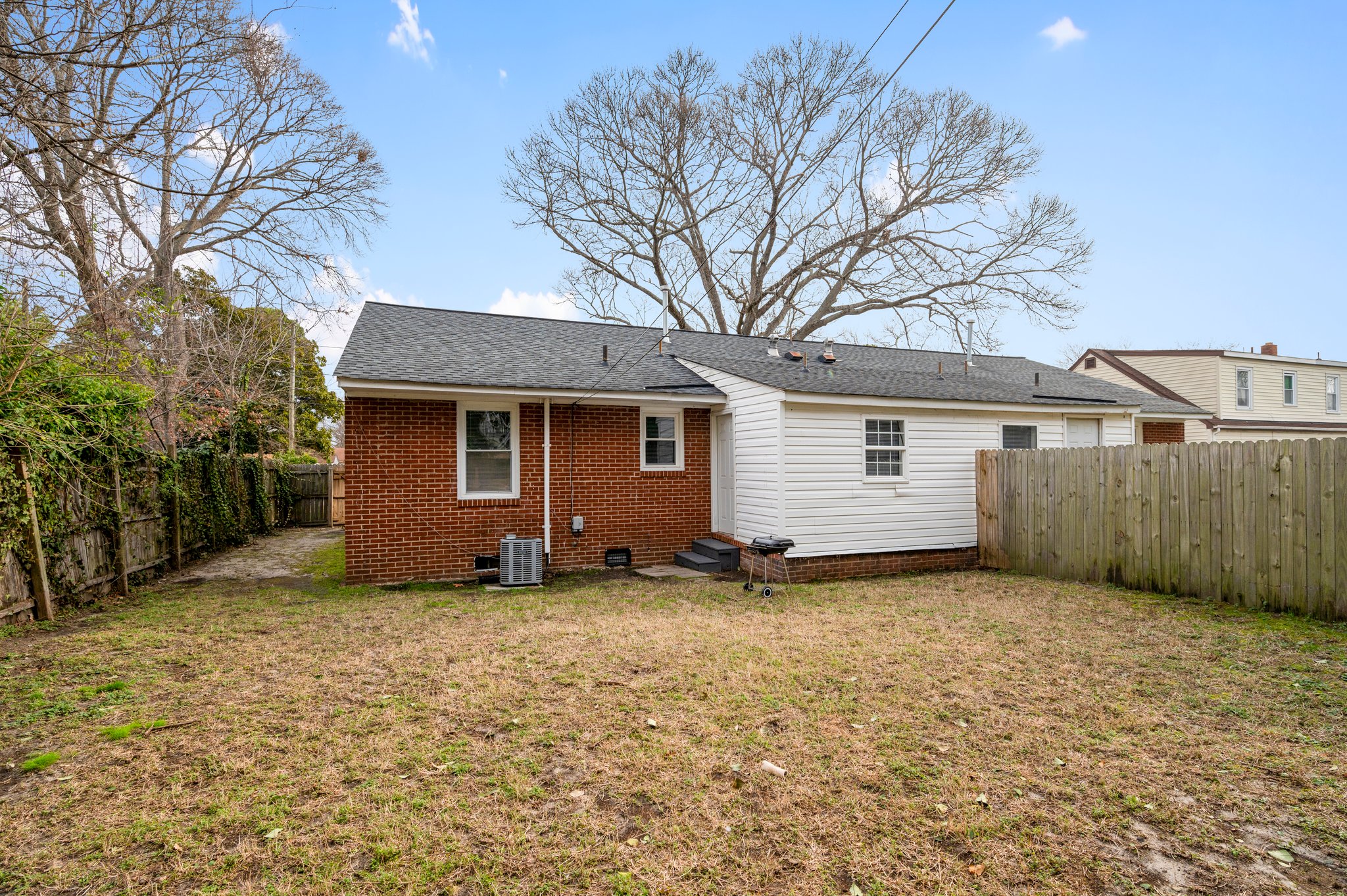 Rear view of a brick duplex with a backyard and wooden fencing.