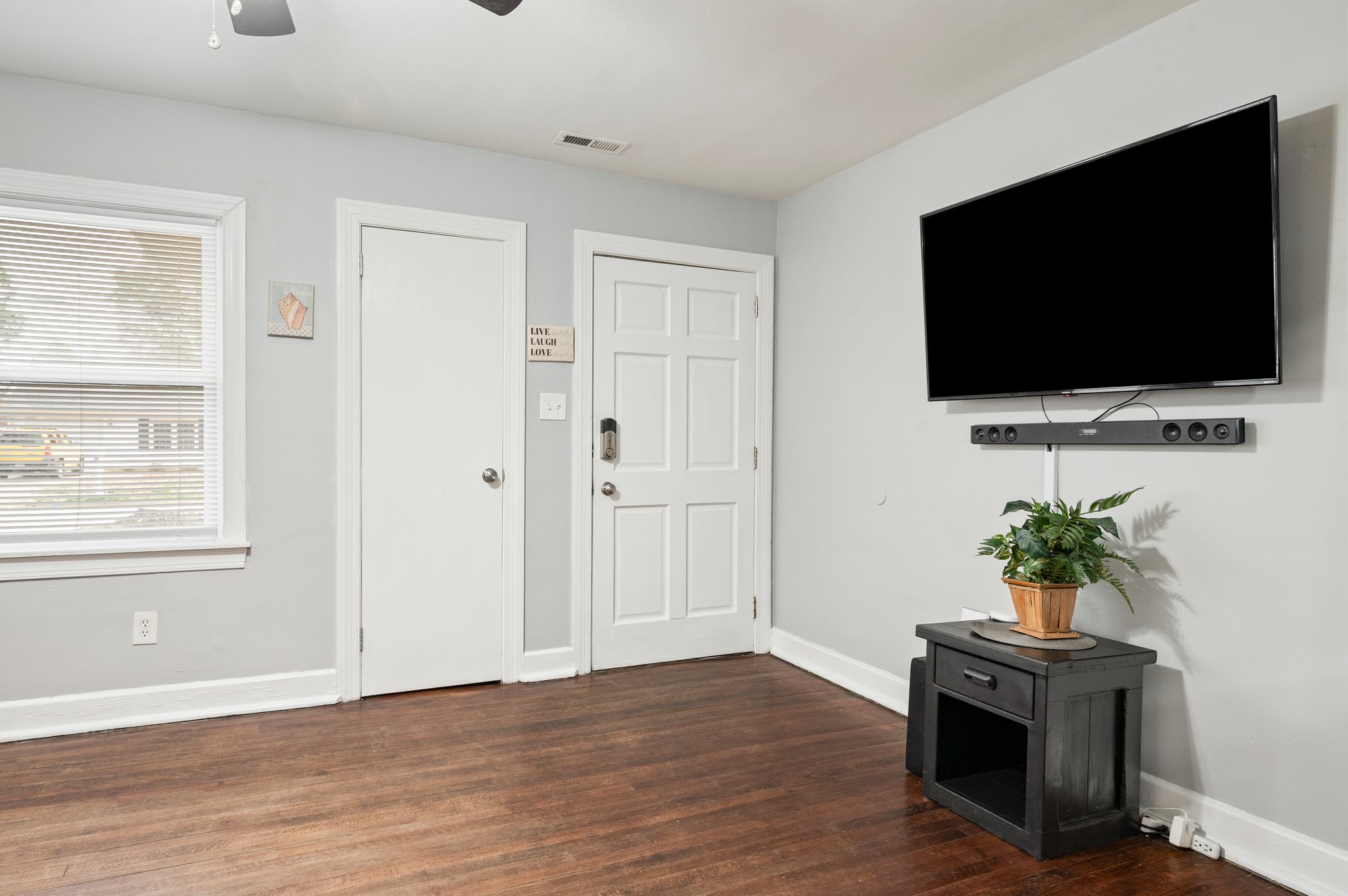 Living room with mounted TV, wooden floors, and a ceiling fan.