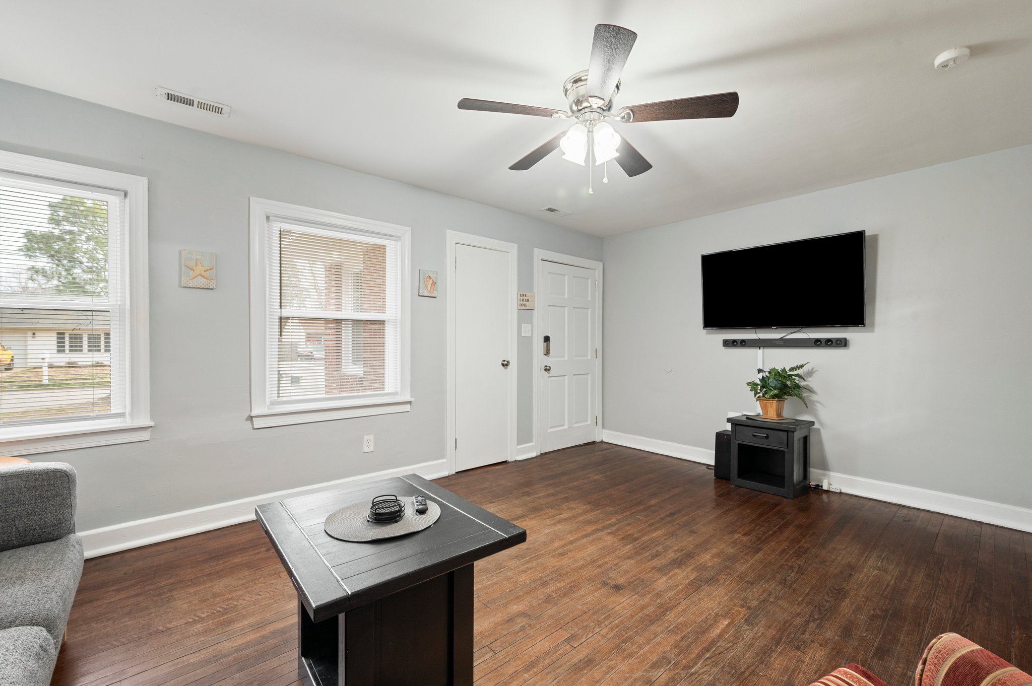 Spacious living room with large windows, TV, and hardwood flooring.