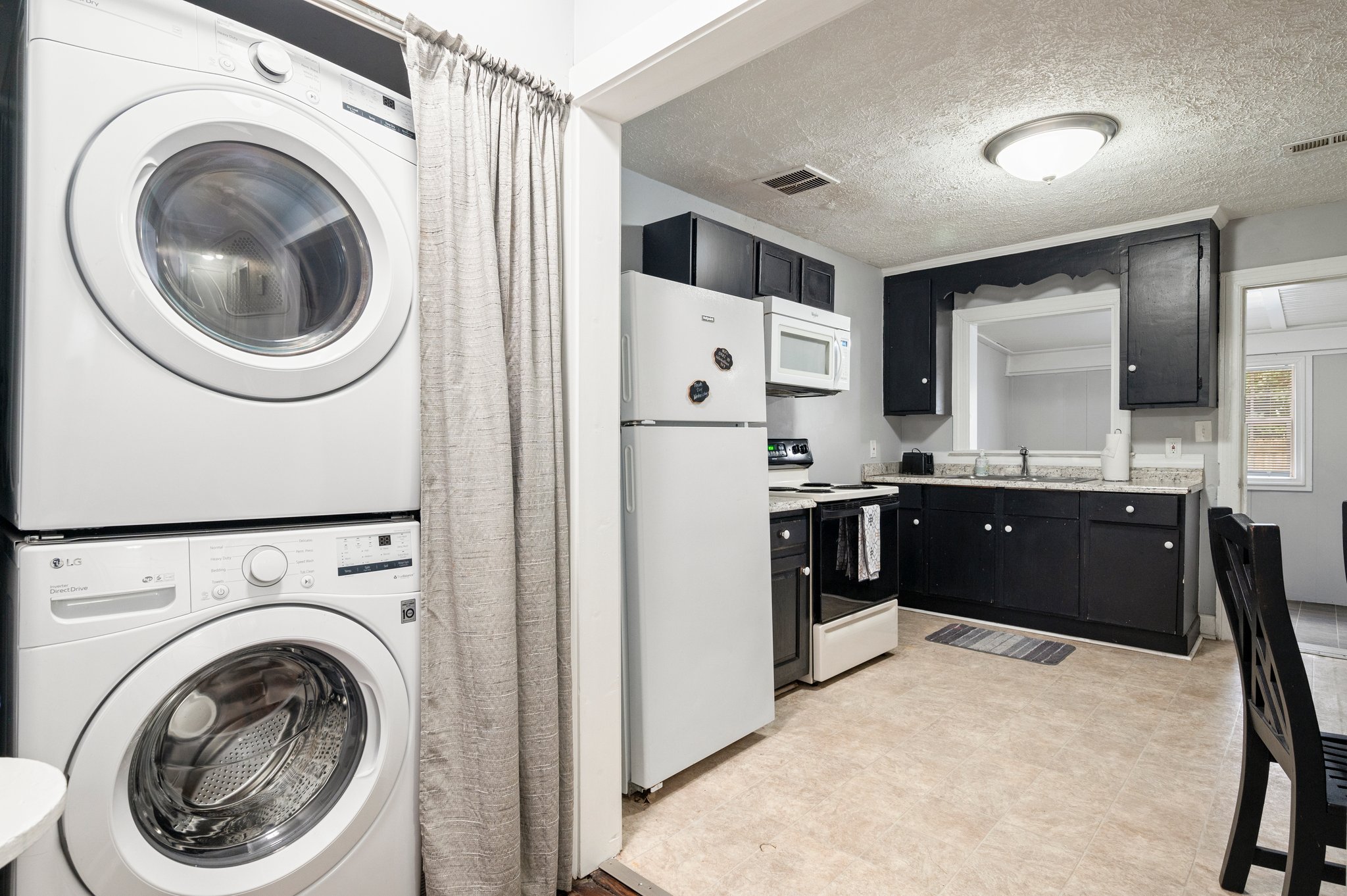 Kitchen with stacked washer and dryer, black cabinets, and white appliances.