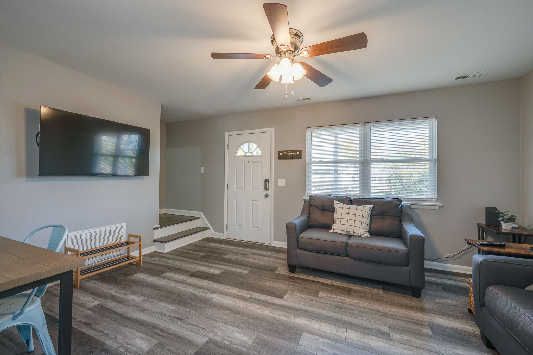 Living room showing front door, gray loveseat, large window, and wall-mounted TV.