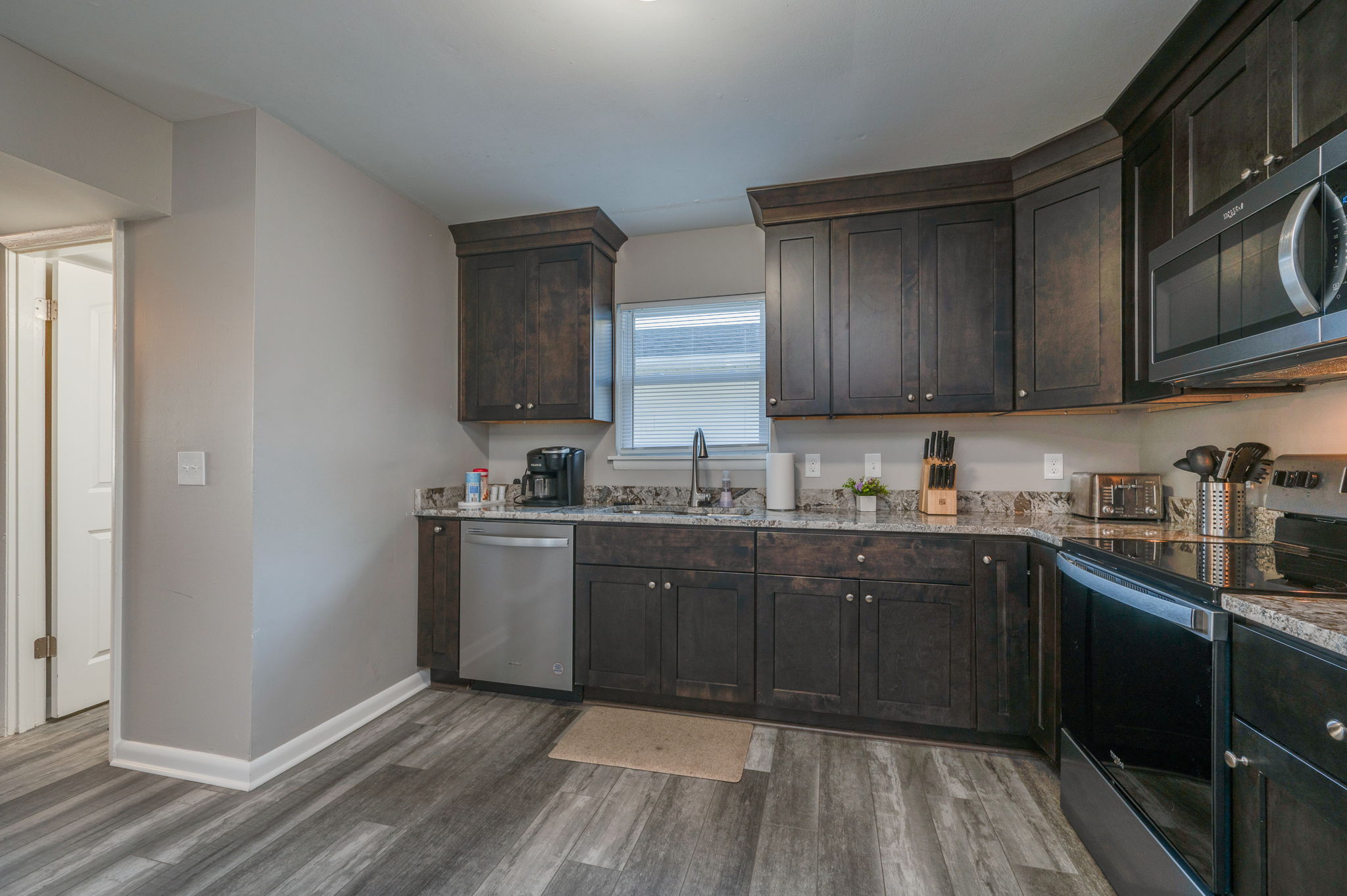 Another angle of the kitchen showing dark wood cabinets, sink, dishwasher, and window.