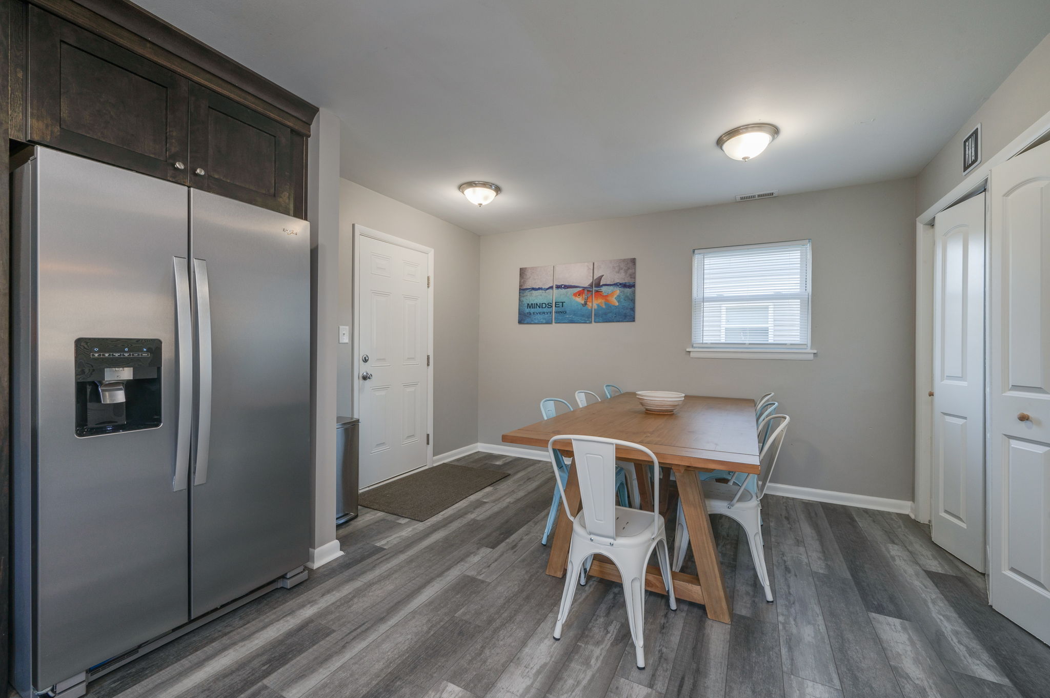 Dining area with large wooden table, light blue chairs, and view into the kitchen.