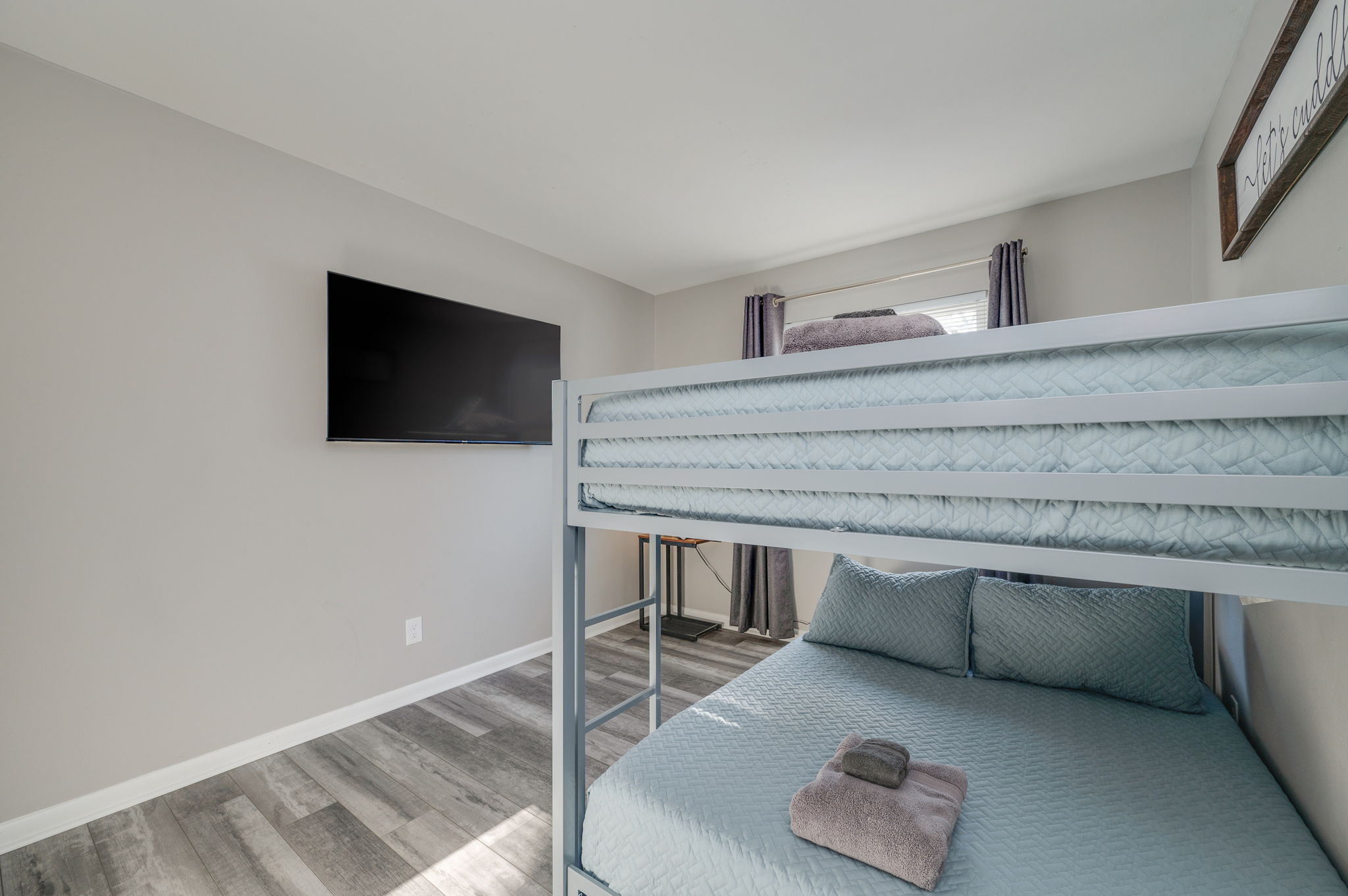 Bedroom with light blue bunk bed, wall-mounted TV, and window with dark curtains.