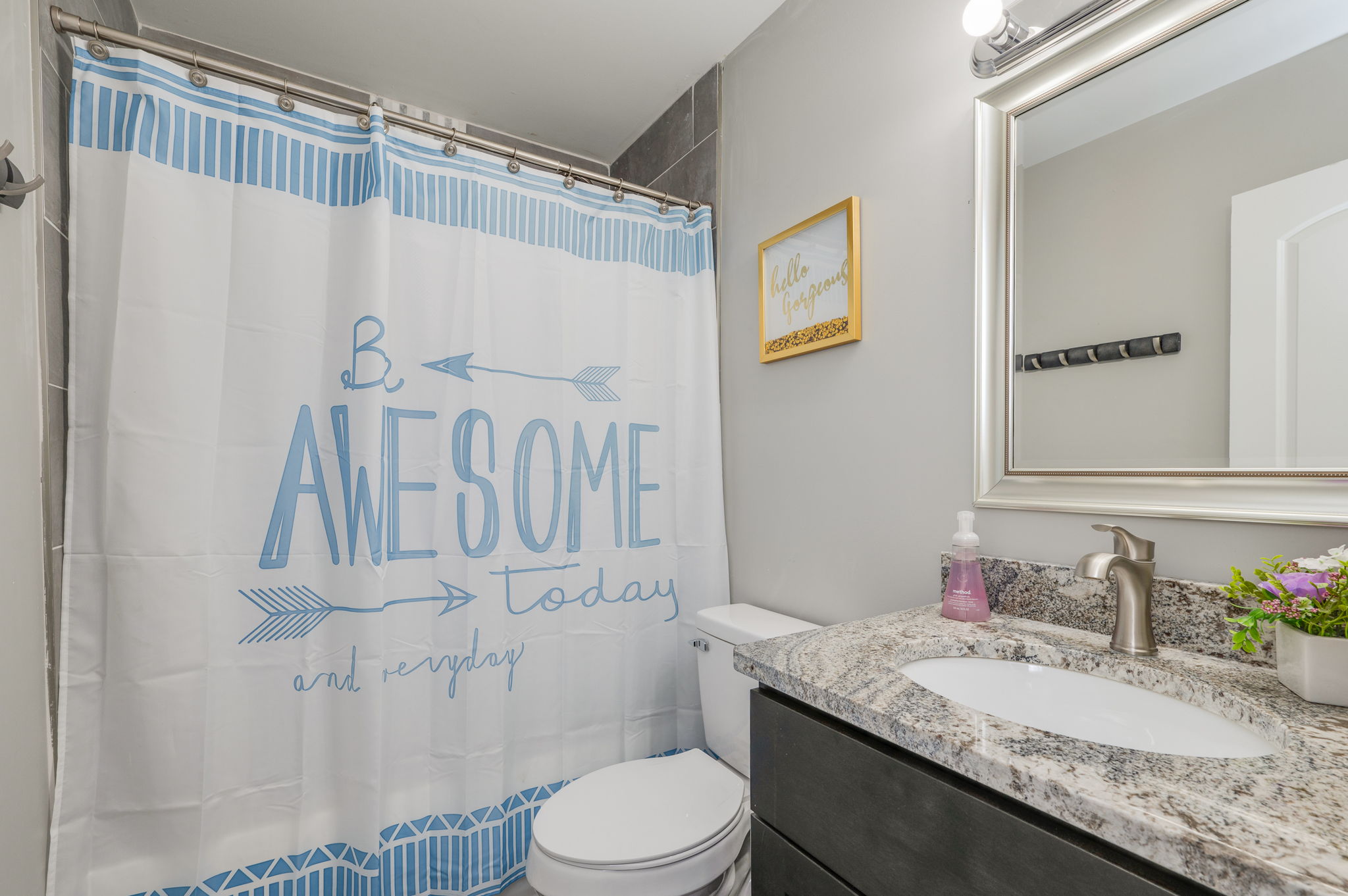 Bathroom with granite countertop, white sink, and shower curtain that says 'Be Awesome Today.'