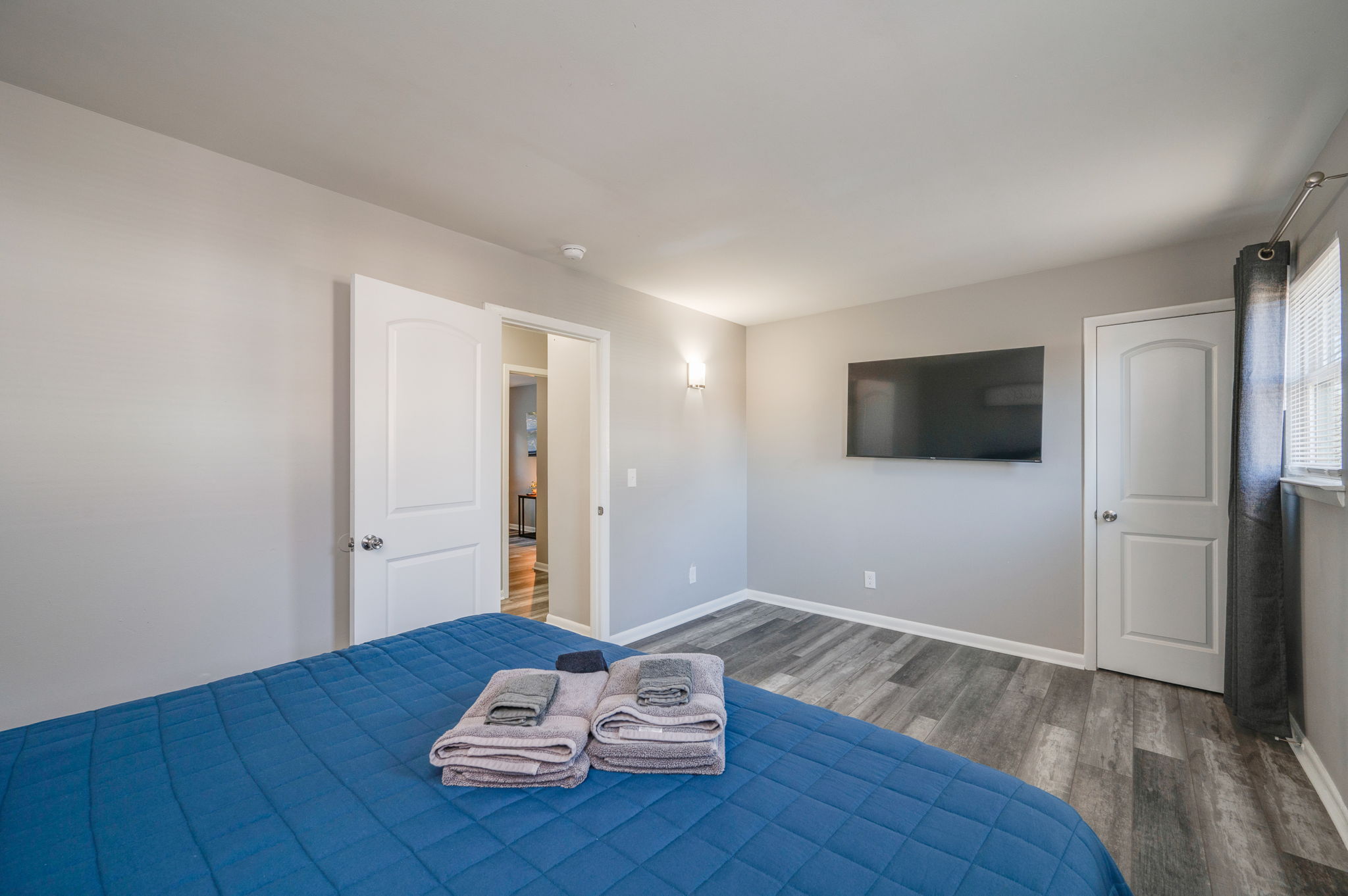 Another angle of the bedroom showing blue bed, wall-mounted TV, and two white doors.